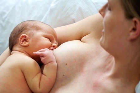 Mutter stillt ihr Baby Haut an Hautin zurückgelehnten Position