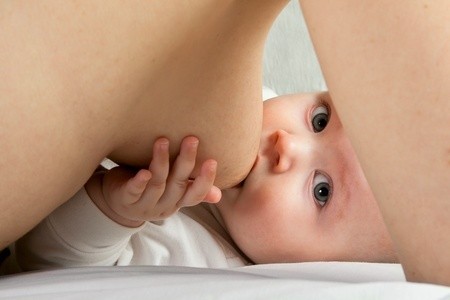 Die Mutter stillt ihr Baby im Vierfüßlerstand.