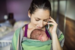Mutter telefiniert mit Baby im Tragetuch