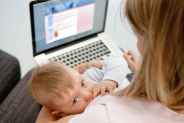 eine stillende Mutter sitzt vor dem Computer und schaut sich die Webseite der La Leche Liga Deutschland an.