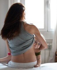 Kleines Mädchen schaut unter dem Arm der Mutter hervor.