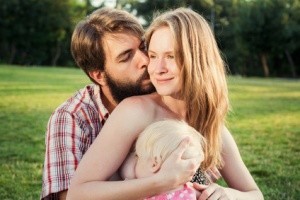 Vater küsst seine Frau, während diese die kleine Tochter stillt.