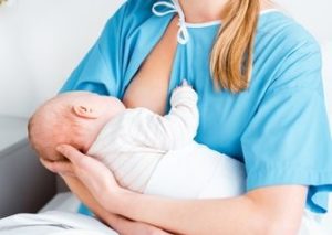 Mutter stillt Baby aufrecht sitzend, Hand stützt den Kopf des Babys.