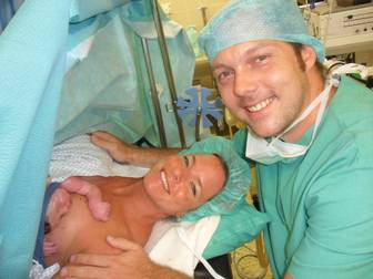 Neugeborenes Baby liegt in einer babyfreundlichen Geburtsklinik an der Brust der Mutter - alle sind in grüner OP-Kleidung nach Kaiserschnitt