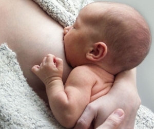 Ein Baby wird gestillt: Es ist in Haut-zu-Haut-Kontakt mit der Mutter, hat viel Brustgewebe im Mund und sein Gesicht ist ganz nah zum Körper der Mutter
