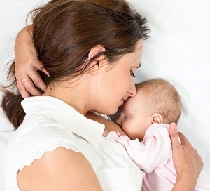 Mutter stillt ihr Baby im Halbschlaf im seitlichen Liegen, das Baby ist ganz nah an ihrem Körper.