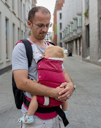 Vater bringt ihr Baby im Babycarrier zum Einschlafen.