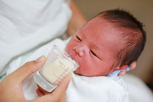 Ein Baby wird mithilfe eines Becher gefüttert.