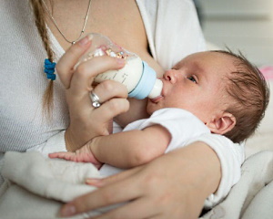 Eine Frau gibt ihrem Baby die Flasche an der nackten Brust