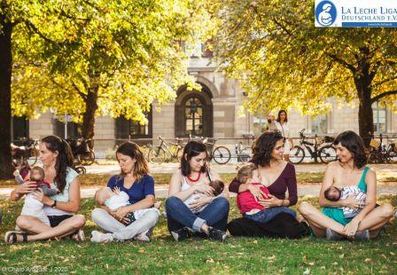 Fünf Mütter einer La Leche Liga Stillgruppe sitzen in einem Park im Schneidersitz und stillen ihre Babys auf ihrem Schoß