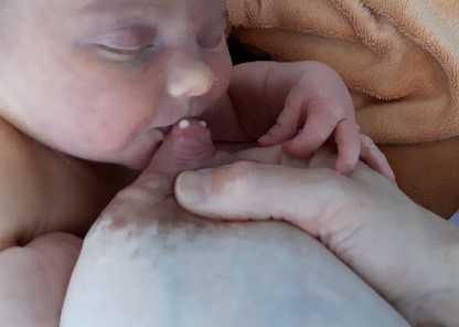 Mutter drückt ihrem schläfrigen Baby Milch in den Mund aus, um es zum Stillen zu wecken