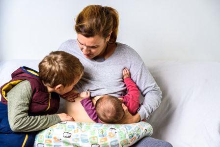 Tandem-Stillen: Mutter stillt ein liegendes Baby und einen stehenden Jungen
