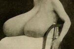 Sitzende Frau mit sehr großen Brüsten, die ihr auf dem Schoß ruhen.